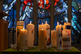 Entzündete Kerzen stehen auf einem flachen Tisch im Altarbereich der Trinitatiskirche. Im Hintergrund ist unschaft das Heiliggeist-Fenster der Trinitatiskirche zu sehen.