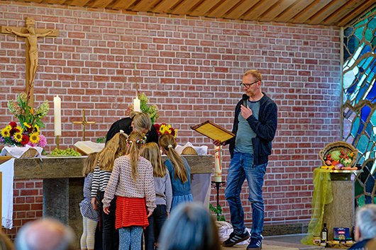 Im reich geschmckten Altarraum sind ein Mitglied des Gottesdienst-Teams mit einer Honigwabe in der Hand, Pfarrerin Mohr und einige Kinder zu sehen.