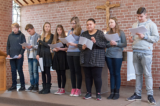 Die Konfirmandinnen und Konfirmanden stehen vor dem Altar und lesen Texte.