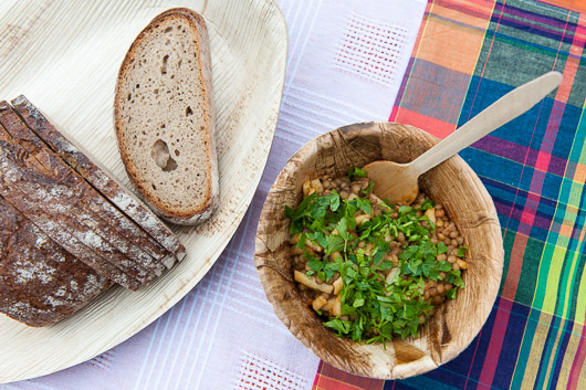 Linsensuppe mit Petersilie in einem Holzschlchen auf einer mit Deckenteilen aus verschiedenen Kirchengemeinden gestalteten Tischdecke.