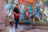 Zwei Mitglieder der Micha-Lokalgruppe mit E-Gitarre und Bassgitarre beim Musizieren vor dem Pfingstfenster der Trinitatiskirche.