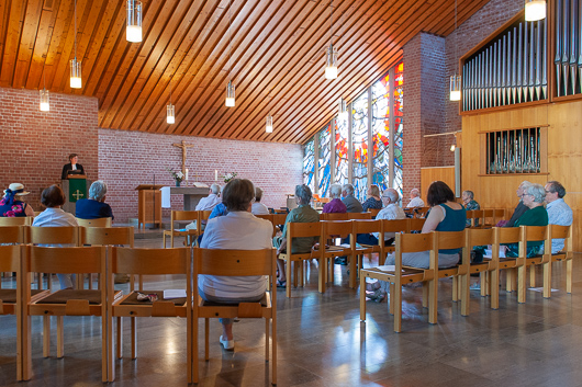 Blick vom Eingang des Kirchenraums in Richtung Altar und Kanzel, wo Pfarrerin Mohr beim Halten der Predigt zu sehen ist.