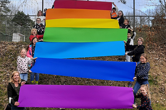 Kinder haben sich an einem Hang im Auenbereich der Trinitatiskirche mit Kreppbahnen in Regenbogenfarben aufgestellt.