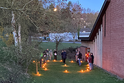 Die Gottesdienstbesucher*innen haben sich auf dem Auengelnde der Kirche im Kreis aufgestellt und geben das Osterlicht weiter.