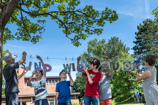 Kinder und 10Plusler bringen beim Gemeindefest die Buchstabenfolge SIND WIR BUNT an einer Leine an.