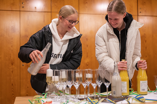 Beim Empfang im groen Gemeinderaum nach dem Gottesdienst schenken wei Konfirmandinnen alkoholfreiem Sekt und Orangensaft in bereitgestellte Glser ein.