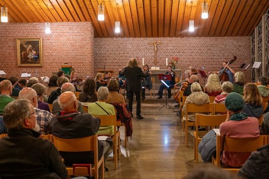 Blick vom hinteren Teil der Kirche ber die Zuschauerreihen in Richtung Altarraum, wo das Kammerorchester der Marburger Philharmonie beim Konzertieren zu sehen ist.