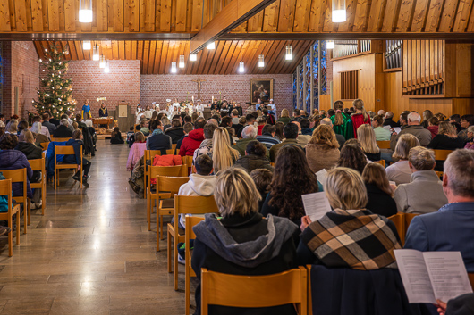 Blick aus dem hinteren Teil des bis auf den letzten Platz gefllten Gottesdienstraums in Richtung Altar, wo ein Groteil der Kinder und Jugendlichen in einer Szene des Krippenspiel zu sehen ist.