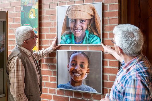 Im Foyer der Trinitatiskirche sind Heinz Rau und Rainer Wagner zu sehen, wie sie zwei bereinander angeordnete Fotos von Kindern des Straenkinder-Projekts ausrichten.