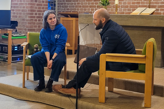 Pfr. Martin Hahn und eine Teilnehmerin des Jugendgottesdienstes sind sich unterhaltend und in Sesseln sitzend im Altarraum der Trinitatiskirche zu sehen.